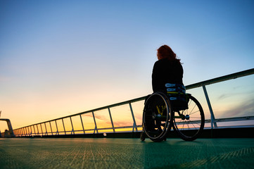 Young woman alone in wheelchair in sunset on a cruise ship deck