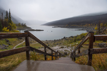 Escaleras de madera que bajan al lago maligne en Jasper Alberta canada en el verano con una tarde nublada con tonos verdes, amarillos y grises.