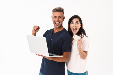 Emotional adult loving couple isolated over white wall background using laptop computer make winner gesture holding credit card.