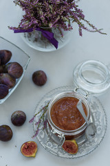 Homemade fig jam in glass jar with fresh purple figs on gray wooden background. Soft focus. Harvesting time or healthy food concept. Top view