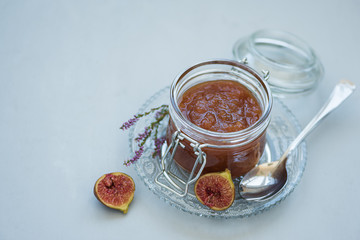 Homemade fig jam in glass jar with fresh purple figs on gray wooden background. Soft focus. Harvesting time or healthy food concept