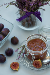 Homemade fig jam in glass jar with fresh purple figs on gray wooden background. Soft focus. Harvesting time or healthy food concept
