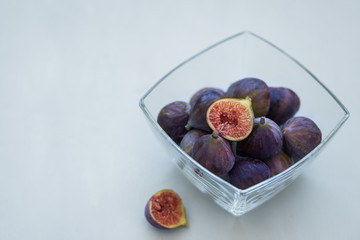 Fresh purple figs in glass bowl on gray wooden background. Soft focus. Harvesting time or healthy food concept