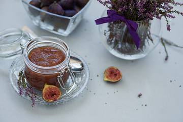 Homemade fig jam in glass jar with fresh purple figs on gray wooden background. Soft focus. Harvesting time or healthy food concept