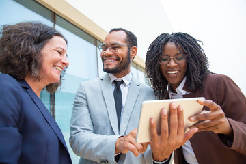Happy business people with digital tablet. Low angle view of cheerful male and female multiethnic business colleagues standing and using tablet pc together. Technology concept