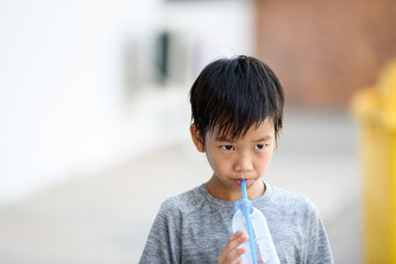 Young boy drink water from plastic straw.