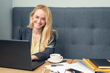 beautiful blonde businesswoman is sitting on sofa and surfing on internet at cafe