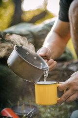 Man traveler hands holding a Cup of tea outdoors. The concept of adventure, travel, tourism and camping. Tourist drinking tea from a mug in the camp