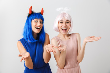 Portrait of two nice happy women wearing toy devil horns and halo laughing at camera