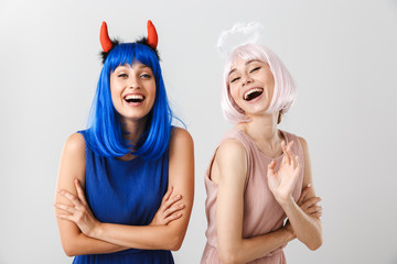 Portrait of two nice young women wearing toy devil horns and halo looking and laughing at camera