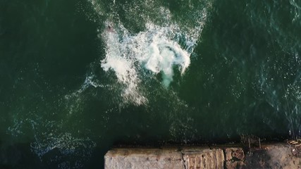 Aerial top view of group of young friends jumping from a pier into the sea during beautiful sunrise