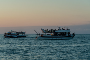 Small pleasure tourist boat sailing from the port for a cruise off the coast on a summer evening against the mountains, Batumi
