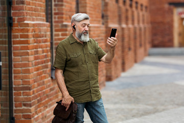 Gray-haired businessman in casual clothes standing in the alley of the business center and talking...