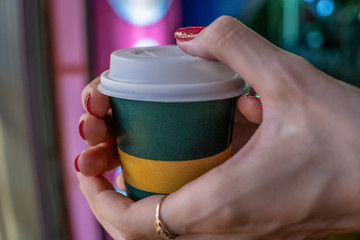 Women's hands with red nail Polish holding a paper Cup of coffee close-up at night