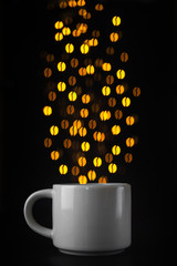 Coffee cup on a dark background, over the cup the lights of a garland in the form of coffee beans. Minimalism, creative coffee concept. Place for text.