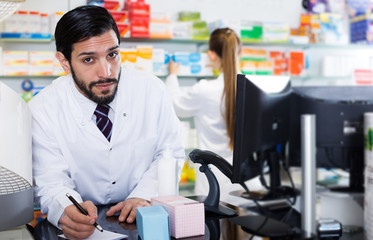 pharmacist is inventorying medicines with computer and paper
