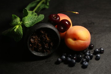bowl with tobacco for hookah. fruits and berries on a black background. smoke hookah