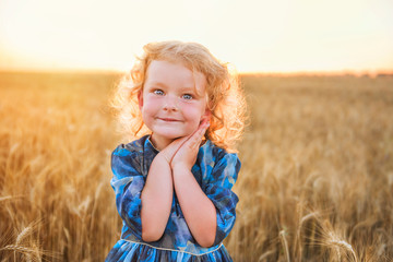 Little cute curly-haired red-haired girl in a golden wheat field in gentle sunlight.
