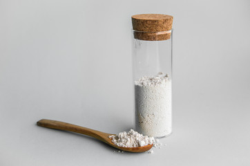 Diatomaceous earth also known as diatomite mixed in glass jar and wood spoon on gray background,...
