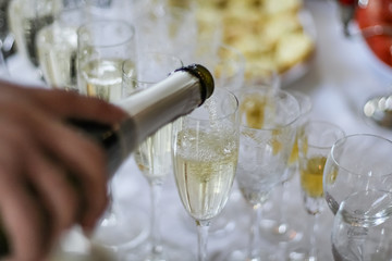 Pouring sparkling wine champagne into tall glasses for a wedding ceremony celebration close up.