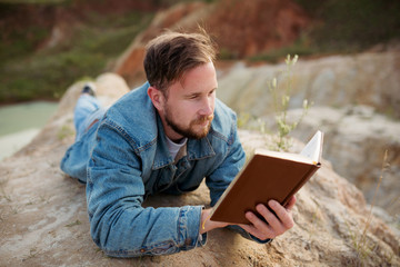 Researcher enthusiastically reading a book lying on the shore of a natural blue lake