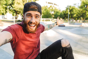 Attractive cheerful young man sitting at the skate park ramp