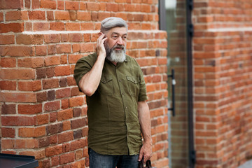 Fototapeta na wymiar Gray-haired adult businessman hipster in casual clothes standing in the alley of the business center and talking on the phone