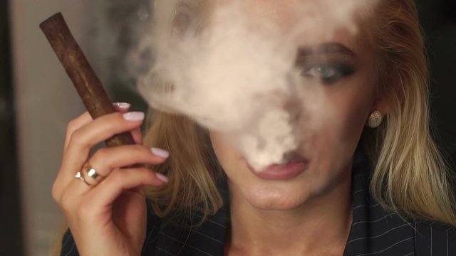 Close-up of a girl Smoking a cigar, she blows a lot of smoke on the camera. Slow motion. Close-up of a sexy woman Smoking a cigar in a bar in a cafe. Slow motion.