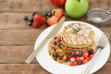 Homemade pancake or hot cake stacked on white plate with fresh fruit and apple raisin sauce on wood table. Pancakes for breakfast or dessert with caramel sauce and sugar icing so sweet and delicious.