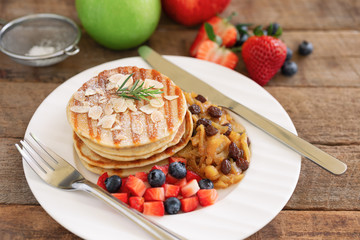 Homemade pancake or hot cake stacked on white plate with fresh fruit and apple raisin sauce on wood table. Pancakes for breakfast or dessert with caramel sauce and sugar icing so sweet and delicious.