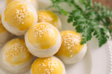 Chinese flaky pastry or mooncake filled sweet mung bean paste and salted egg yolk on white plate decorated with white sesame in close up view macro concept to present detail. Homemade bakery concept.