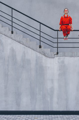 Young woman in red overalls and red sunglasses posing on the gray stairs. Industrial concept
