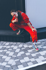 Young woman in red overalls and red sunglasses posing near grey and black wall with candy