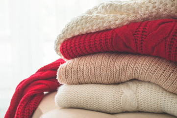Obraz na płótnie Canvas A stack of knitted sweaters in the interior of the living room. The concept of autumn winter comfort