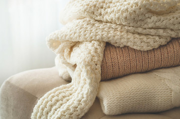 A stack of knitted sweaters in the interior of the living room. The concept of autumn winter comfort