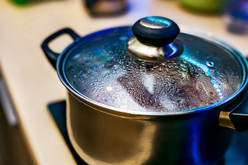 Metal pan with misted lid. Water droplets on the dishes during cooking on the electric stove. Close...