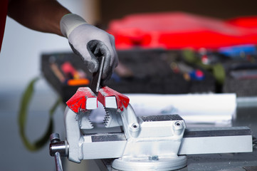 In the photo, a hand in a gray work glove puts a metal workpiece in tees for subsequent processing