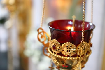 The Orthodox Church. Church lamp with lighted candle and red glass in gold case hanging in front of icons