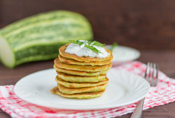 fresh delicious zucchini pancakes with sour cream and herbs on the table