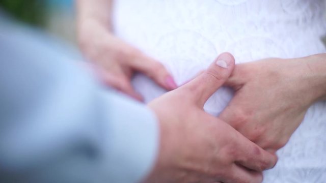 A pregnant girl holds her hands on her stomach. Four hands on the pregnant woman's stomach. A heart made of fingers on a pregnant woman's stomach.