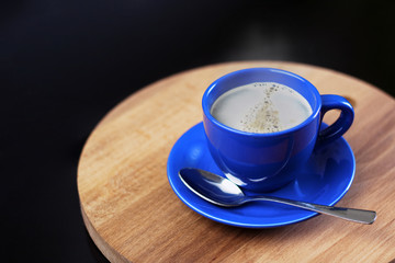A Cup of fresh coffee on a wooden stand. Steam from a coffee mug. Coffee foam. Blue mug with a hot drink on a dark background.