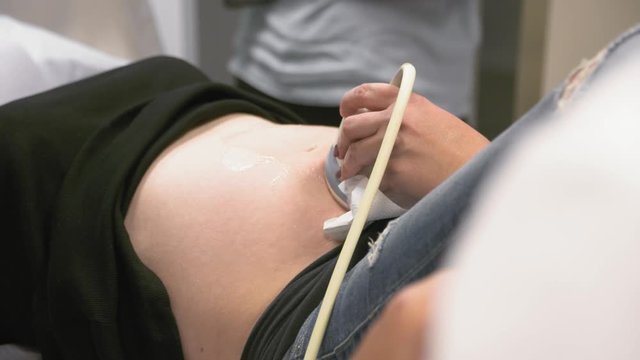 Ultrasound scanner on a second trimester pregnant woman's belly, close up