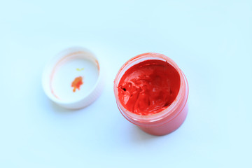 Open jar of red gouache, light background.