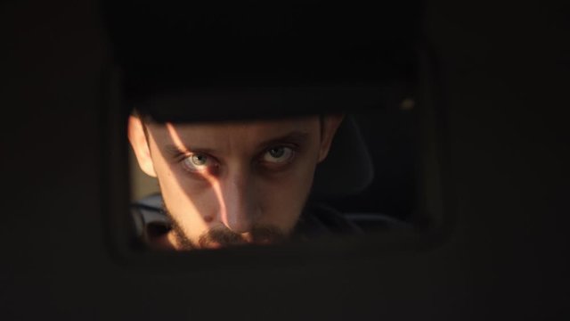 man looks at himself in a mirror while sitting in a car