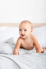 Cute little child crawling on white bedclothes and looking away