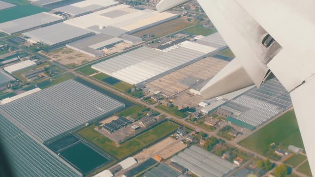 The plane is preparing for landing. Flying over water channels, greenhouses, farms with solar panels, houses, the route of the city of Amsterdam, Holland, the Netherlands