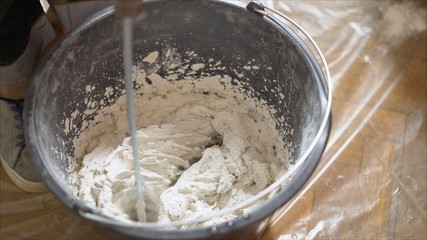 Mix the solution in a bucket using a construction mixer. Worker mixing plaster in a bucket for alignment and putty walls of the apartment using an electric drill, close-up.