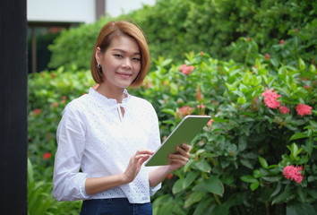 Portrait of a woman standing holding a tablet. Smiling woman at green outdoor with copy space