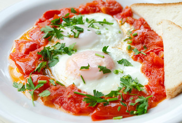Fried eggs with sliced tomatoes and parsley on the plate. Roasted eggs close up. Healthy breakfast and lunch.