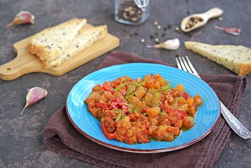 Vegetable ratatouille or stew of zucchini, sweet pepper, carrots and tomato on a blue plate on a dark brown concrete background. Vegetarian food. Autumn harvest. Thanksgiving Day.